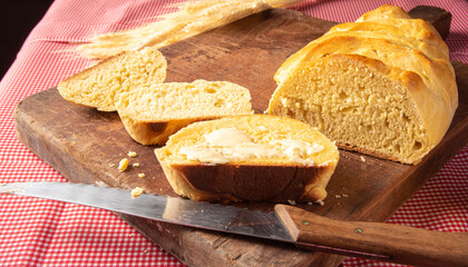 Homemade bread, sliced ​​homemade bread with butter on wood and a red and white checkered tablecloth, a knife and a bunch of wheat, selective focus.