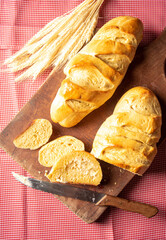 Homemade bread, sliced ​​homemade bread with butter on wood and a red and white checkered tablecloth, a knife and a bunch of wheat, selective focus.