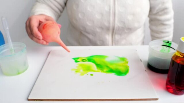 woman applies green paint with an eyedropper, inflates it, abstract spots spread over a white surface, drawing with watercolors, alcohol ink, background for a designer, art therapy