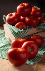 Tomatoes, beautiful tomatoes arranged in a basket and on wood, with a green and white checkered tablecloth, dark background, selective focus.