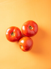Tomatoes, three tomatoes arranged on an orange surface, top view.