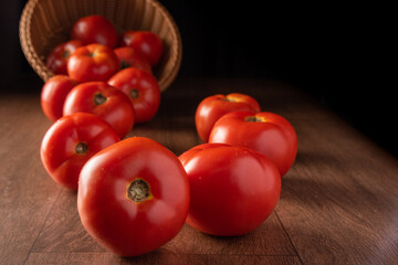 Tomatoes, beautiful tomatoes falling out of a basket on wooden surface, dark background, selective...