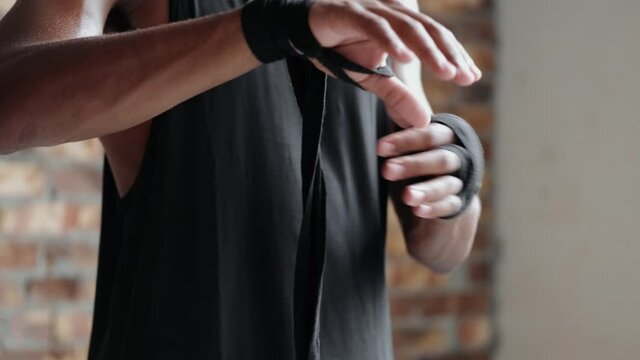 A cropped view of a sportsman is putting on bandages for boxing while training indoors