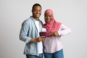 Smiling couple holding flying tickets and passports over grey background