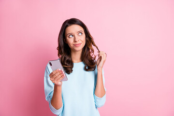 Photo of young girl happy smile dream dreamy look empty space use cellphone browse isolated over pink color background