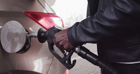 Cropped close up image of unrecognizable African businessman in casual wear, rholding in hand filling gun and refueling his luxury car with gasoline at the petrol station - Powered by Adobe