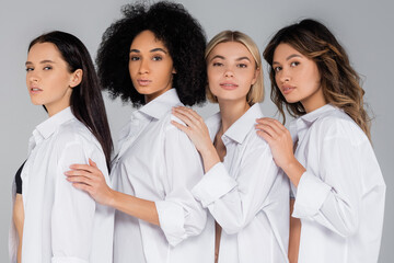 young interracial women in white shirts looking at camera on grey
