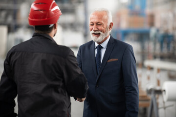 Architect and worker working on project. Colleagues handshake in factory