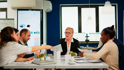 Start up team meeting with company leader planning financial strategy, analysing reports sharing paperwork. Colleagues working in office at conference table in startup management company