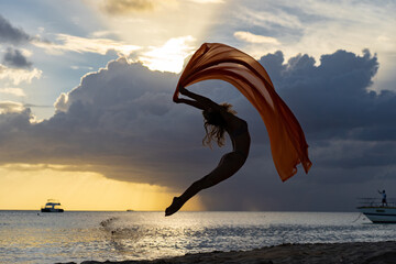 Flexible fit woman jumping with silk during dramatic sunset with stormy clouds. Concept of...