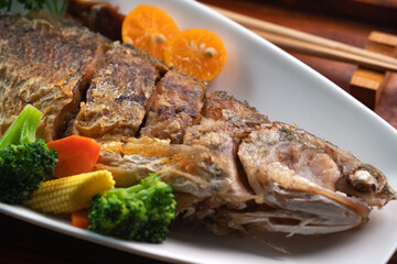 Close up of delicious pan-fried fish dish in a white plate with vegetable.