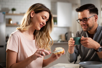 Beautiful woman enjoying in breakfast with boyfriend. Happy young couple drinking coffee and eating sandwich at home.