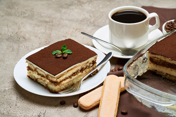 Traditional Italian Tiramisu dessert in glass baking dish and portion on grey concrete background