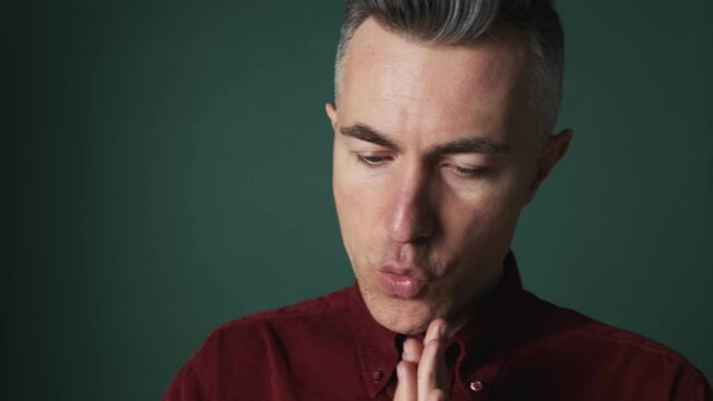 A close-up view of a nervous elder man is doing winner gesture standing isolated over green background in the studio