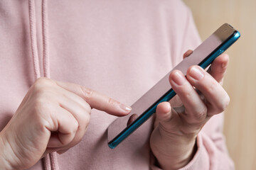 Woman wearing a nude sweater is using mobile phone or smartphone. Close up