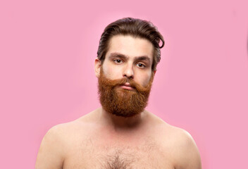 Obraz premium Young handsome strong man with beard shirtless standing over isolated pink background, looking at the camera.