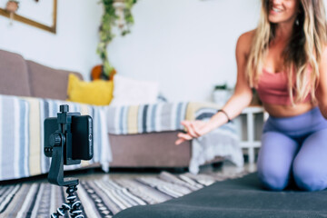 Young woman exercising at home doing workout and recording at her with cellular phone to teach...