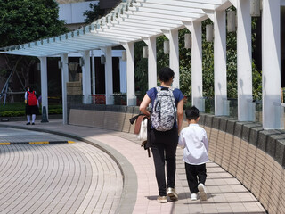 Mother or domestic helper picks up son or kid of primary school student, carrying school bag return...