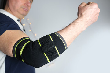 close-up of a man's elbow, part of a European's hand in a black elastic bandage, elastic roller Compression bandage concept of fixing an injured limb