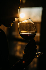 Silhouette of a young woman holding a glass of red wine in sunset light at a restaurant.