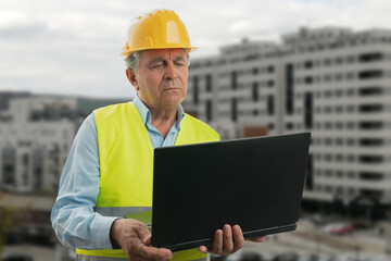 Elderly builder man with focused expression looking at laptop