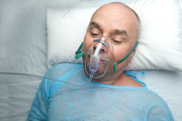 elderly man patient in a blue shirt lies in a facial oxygen mask, the concept of medical care,...
