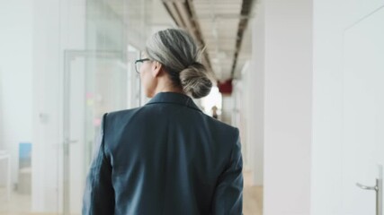 A back view of an elder businesswoman is walking through the corridor in the office building