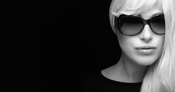 Beautiful blond woman in sunglasses with long silver white hair, looking at camera. Monochrome close-up fashion portrait isolated on black background with copy space for text