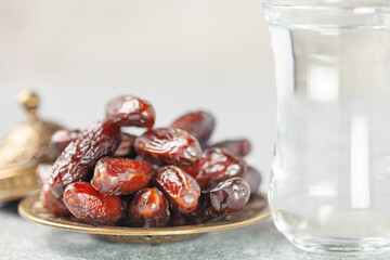 A glass of water and dry dates on saucer ready to eat for iftar time. Islamic religion and ramadan concept.