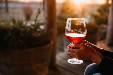 Female hands holding a glass of red wine outdoors in sunset light.
