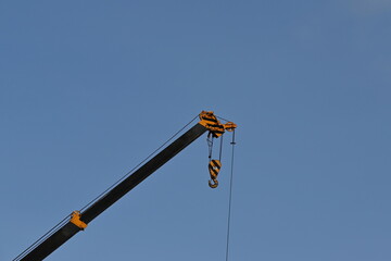 Hooks with steel crane slings and arms painted in yellow and black on a blue sky background. Used for lifting large objects or items weighing up to 25 tons.
