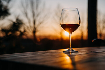 Glass of red wine on a wooden table at a terrace at sunset.