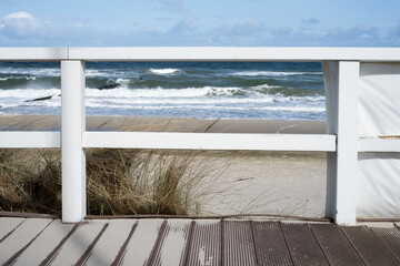 White wooden veranda on the Baltic Sea beach with waves, sand, blue sky and sun