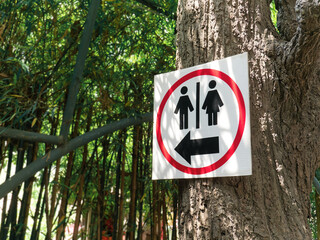 Black Toilet Sign with Arrow Inside Red Circle Hanging on the Tree