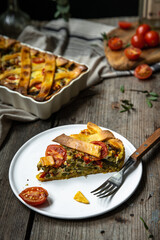 Piece of freshly baked savory pie (quiche) with green beans, peas, bell pepper, cherry tomatoes and cheese  on white plate on rustic wooden table.