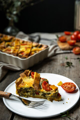 Piece of freshly baked savory pie (quiche) with green beans, peas, bell pepper, cherry tomatoes and cheese  on white plate on rustic wooden table.