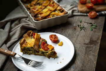 Piece of freshly baked savory pie (quiche) with green beans, peas, bell pepper, cherry tomatoes and cheese  on white plate on rustic wooden table.