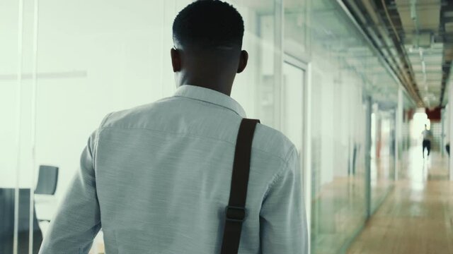 A back view of a american guy is walking down the hall inside the office building