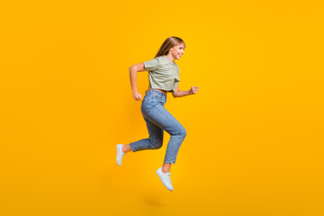 Full length body size profile side view of attractive cheerful teen girl jumping running active motion isolated over bright yellow color background