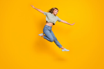 Full length body size view of lovely cheerful girl jumping having fun flying like aircraft isolated over bright yellow color background