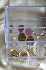 Transparent jewelry box filled with gold earrings and rings. Selective focus.