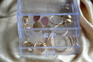 Transparent jewelry box filled with gold earrings and rings. Selective focus.