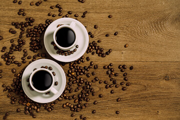 Top view of two white coffee cup over a wooden table with scattered coffee beans.  Flat lay photo with copy space.