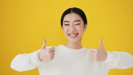 A happy asian woman is pointing at herself standing isolated over yellow wall in the studio