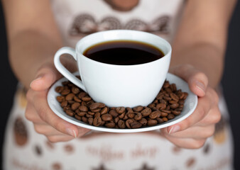 Ceramic cup and coffee beans in female hands on a black background.
