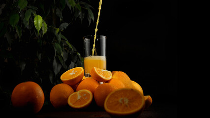 Orange juice is poured into a glass. Ripe oranges on a dark background.