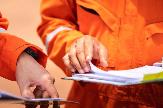 A worker in orange coverall uniform is opening documents to make a discussion on working procedure, safety audit in operation action photo. Close-up and selective focus on human's hand.