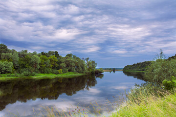 Fototapeta na wymiar A river with overgrown banks in cloudy calm weather