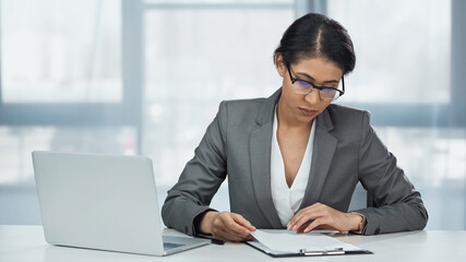 african american businesswoman in glasses looking at papers on clipboard near laptop