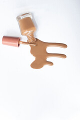 Liquid nail polish with applicator and container, poured out onto a white backdrop